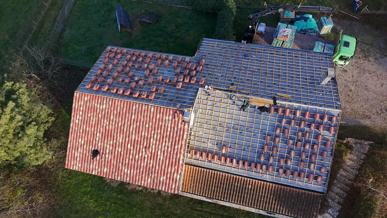 Chantier de rénovation vu du ciel : une partie en tuiles neuves, une partie en cours